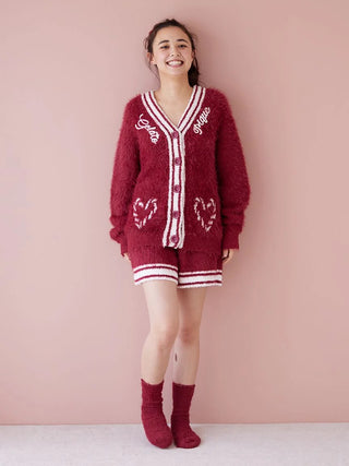 Person wearing a cozy red fuzzy cardigan set with matching socks and shorts, standing against a pink background.