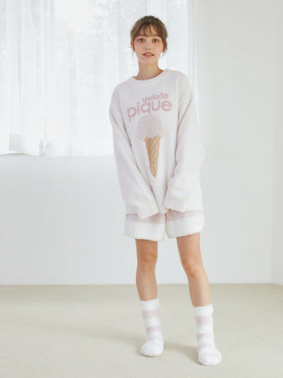 Woman wearing Gelato Pique plush lounge shorts and sweater with cute ice-cream design, standing in a bright room.