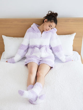 Person wearing fluffy, striped loungewear in pastel shades, relaxing on a bed with a wooden headboard.