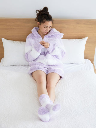 Woman wearing fluffy Gelato 3 Border Lounge Shorts in pink and white, sitting on bed, showcasing cozy and stylish loungewear.