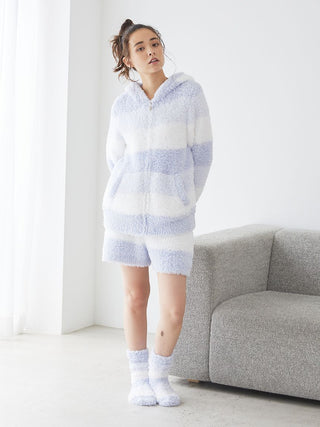 Model wearing soft, fluffy Gelato 3 Border Lounge Shorts and hoodie in pastel shades, standing near a sofa, showcasing comfort and style.