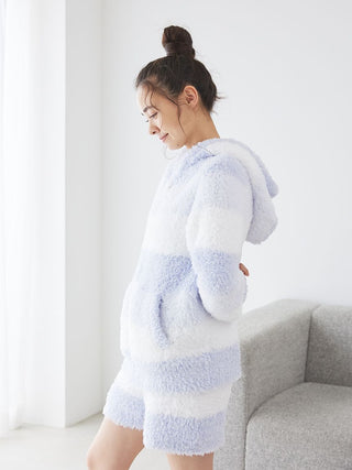 Woman wearing fluffy Gelato 3 Border Lounge Shorts in soft pink and white, standing by a grey sofa, showcasing cozy home loungewear.