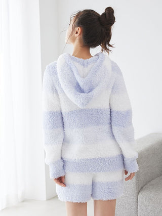 Woman wearing blue and white striped fluffy hoodie and lounge shorts indoors, standing by a sofa.