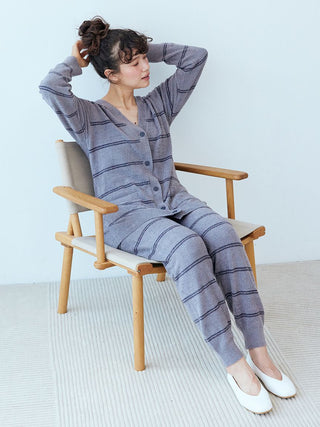 Woman wearing striped knit lounge pants and cardigan, seated on wooden chair, adjusting her hair. Cozy homewear in a relaxed setting.