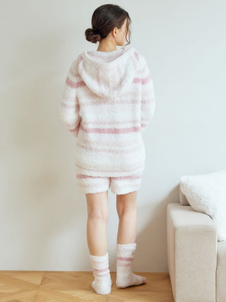 Woman wearing Gelato Random Border Lounge Shorts in fluffy soft pink with matching hoodie and socks, standing by sofa.