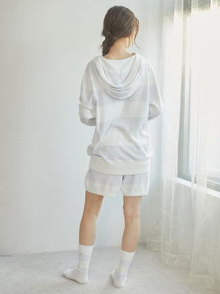 Woman wearing Smoothie 2-Border Lounge Shorts and sweater, standing by a window in cozy home setting.
