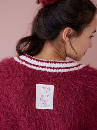 Back view of red feather-textured cardigan with white ribbed collar trim and patch reading 'I WANT TO SLEEP BESIDE YOU'.