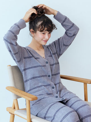 Woman wearing Hot Smoothie Border Cardigan in striped pattern, sitting on a chair, adjusting her hair.