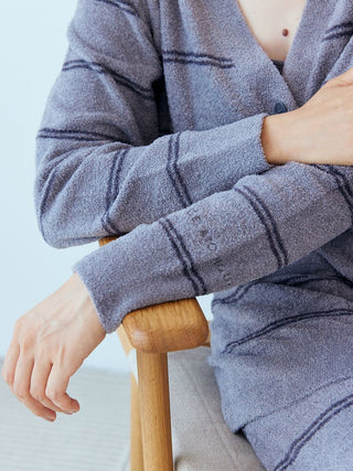 Person wearing Gelato Pique Hot Smoothie Border Cardigan with stripe patterns, sitting on a wooden chair.