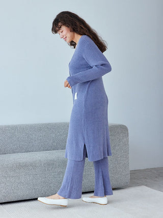 Woman wearing a blue Hot Smoothie Ribbed Long Cardigan, showcasing its sleek silhouette and soft ribbed texture, standing beside a gray couch.