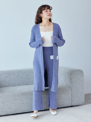 Woman wearing Hot Smoothie Ribbed Long Cardigan in blue, styled with matching pants, standing by a gray couch in a minimalist room.