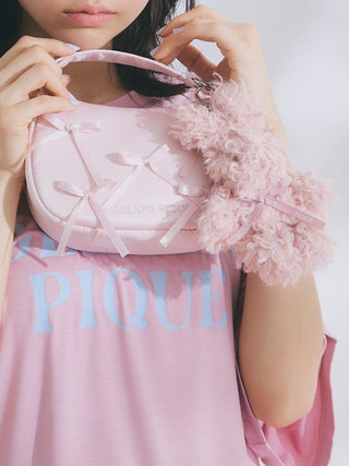 Woman holding Gelato Pique Ribbon Handle Pouch with soft pink design, featuring elegant bows and plush accessory.