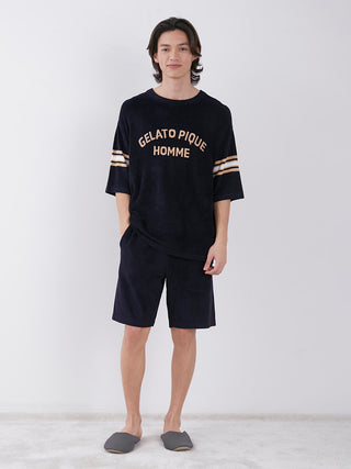Man wearing Gelato Pique Homme black lounge set with sporty shorts, stylish embroidered shirt, and comfortable slippers.
