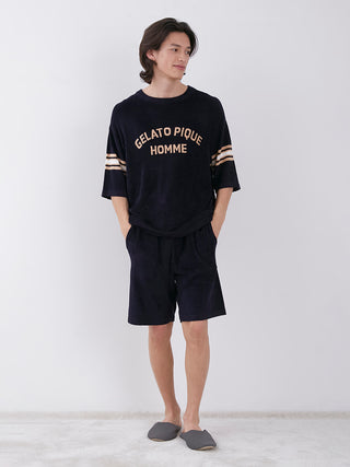 Man wearing Smooth Light Loungewear Shorts with sporty waistline, navy top, and slippers standing against a white background.