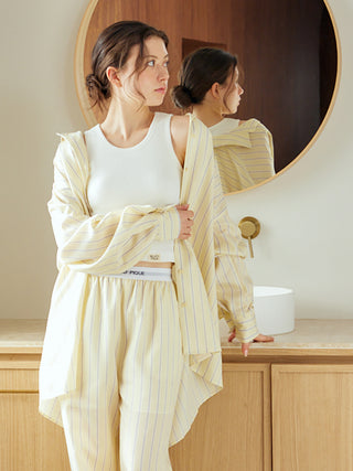 Woman wearing striped long sleeve pajama shirt with relaxed elegant design, silky texture, standing by a mirror in a stylish room.