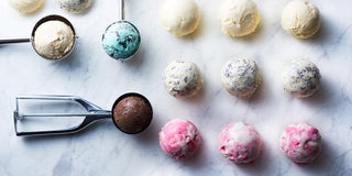 Assorted scoops of ice cream in various flavors placed on a marble surface with ice cream scoops