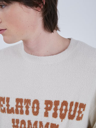 Close-up of a person wearing a cream-colored loungewear top with textured brown lettering, capturing modern, casual style.