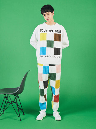 Man wearing EAMES Air Moco Logo Men's Knit Pullover with colorful patchwork design against a green background.