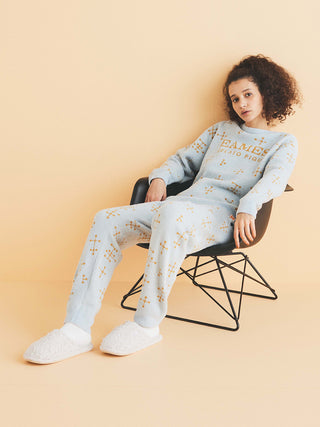 Woman wearing EAMES Cozy Pullover Sweater and pants with iconic dot pattern, seated in black chair, on light background.
