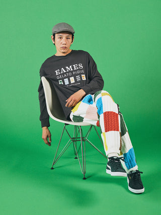 Man wearing EAMES Gelato Pique long sleeve tee and multicolored pants, sitting on a modern chair against a green background.