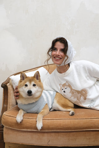 Woman in white Shiba Inu pullover lounging on couch with Shiba Inu dog wearing light blue sweater, highlighting premium comfort loungewear.