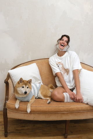 Woman wearing white Shiba Pullover & Shorts Loungewear Set sitting on a sofa with a Shiba Inu dog, showcasing cozy premium loungewear.