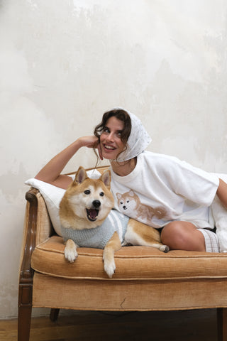 Woman in a white Shiba Inu pullover lounging with a Shiba Inu dog on a couch, showcasing playful comfort in premium loungewear by Gelato Pique USA.