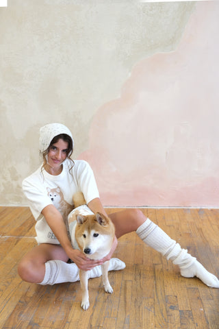 Woman in cozy white Shiba Pullover & Shorts Loungewear Set from Gelato Pique USA, sitting on wooden floor with Shiba Inu dog.