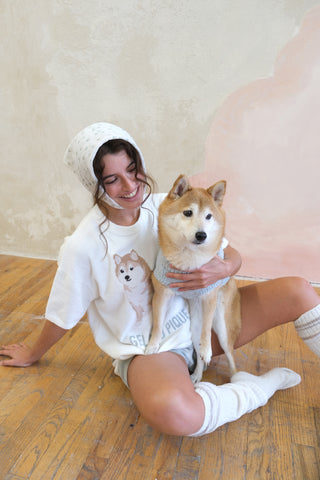 Woman in white Shiba Inu pullover sitting on the floor with a dog, wearing premium loungewear from Gelato Pique USA.