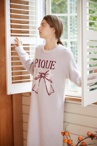 Woman wearing Gelato Pique Ribbon Jacquard Dress with burgundy ribbon motif, standing by window with shutters open.