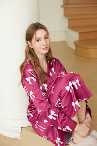 Woman wearing Ribbon Pattern Satin Shirt Dress in vibrant bow print, seated indoors with a casual and relaxed pose.