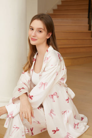 Woman wearing a Ribbon Pattern Satin Shirt Dress with pink bow prints, sitting gracefully indoors on wooden stairs.