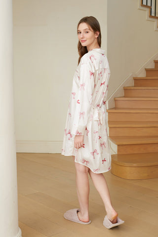 Woman wearing Ribbon Pattern Satin Shirt Dress with bow print, showcasing elegant loungewear style in a home setting.