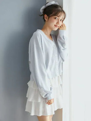 Woman wearing Airy Moco Tiered Mini Skirt with a light blue sweater, standing by a window, showcasing soft and elegant loungewear.