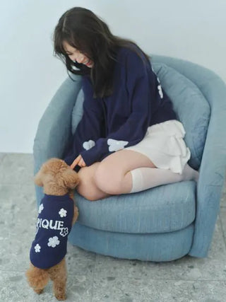 Woman sitting on a chair wearing the Airy Moco Tiered Mini Skirt, playing with a small brown dog dressed in a blue sweater.