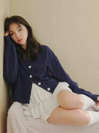 Woman wearing a white Airy Moco Tiered Mini Skirt and navy cardigan, sitting comfortably indoors on a cozy chair.