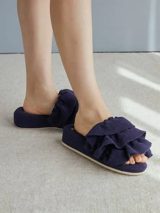 Woman wearing navy Airy Moco Tiered House Slippers with plush tiered design for comfort and style on carpeted floor.