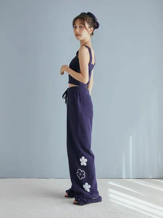 Woman wearing navy lounge set with floral accents and hair tied up against a light backdrop.