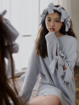 Young woman wearing a Plush Bow Hair Ribbon and cozy sweater, reflecting elegance and charm, sitting in a stylish room.