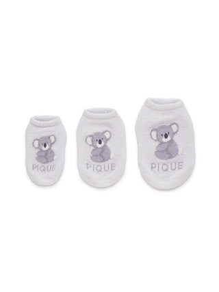 Three sizes of white fluffy socks with koala bear design for children, labeled PIQUE.