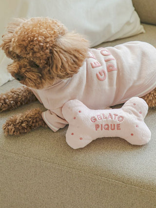 Poodle wearing a pink outfit on a couch with a bone-shaped plush toy labeled 'Gelato Pique'. Perfect for cats and dogs.