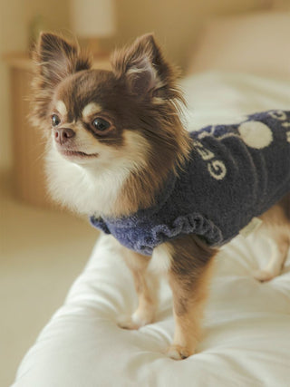 Small dog wearing a CAT & DOG Smoothie Cherry Jacquard pet sweater standing on a white bed.