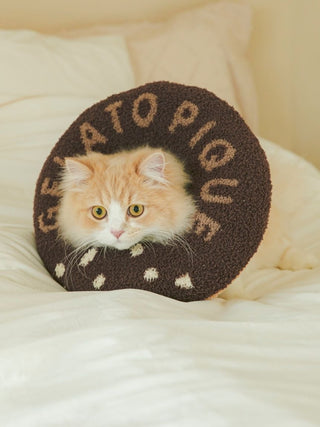 Fluffy cat wearing a brown and beige donut-shaped pet neck pillow on a bed.