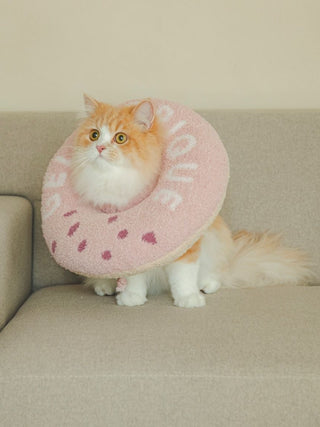 Fluffy cat wearing a pink Moco Donut pet neck pillow on a couch, designed for cat and dog comfort.