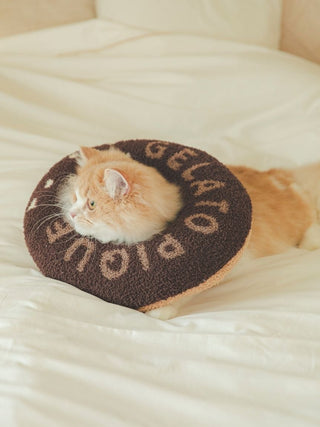 Cat wearing a cozy, premium Gelato Pique USA brown donut neck pillow on a bed, perfect for pet loungewear comfort.