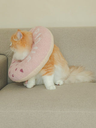 Orange cat wearing pink CAT & DOG Baby Moco Donut Pet Neck Pillow on beige couch. Cozy, premium pet loungewear by Gelato Pique USA.