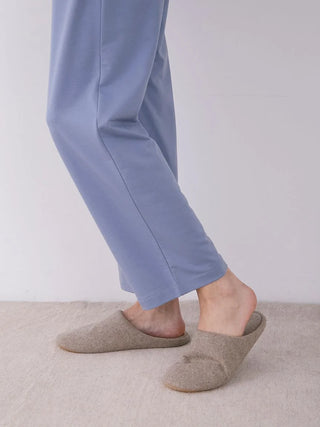 Side view of a person wearing blue lounge pants with star pattern and gray slippers, standing on a light carpeted floor.