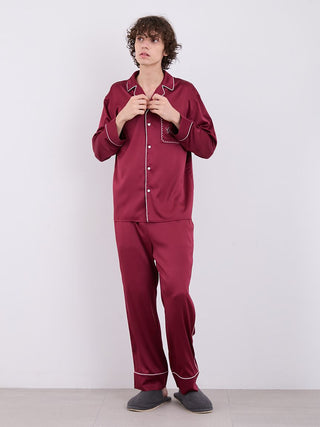 Man wearing burgundy satin pajama pants with white piping, showcasing luxurious comfort and style for restful nights.