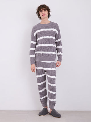 Man wearing gray and white striped Aran cable knit pajama pants and matching sweater, standing against a neutral background.