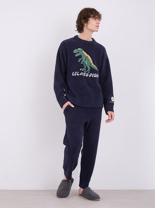 Man wearing Gelato Pique Powder Dinosaur Jacquard Lounge Pants and dinosaur sweater in a cozy home setting.